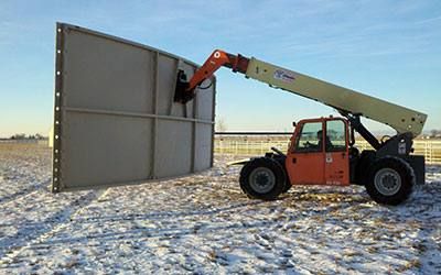 A telehandler holding a single tank panel upright on a snow-covered site.