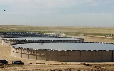 A long row of filled modular tanks on an open prairie location.